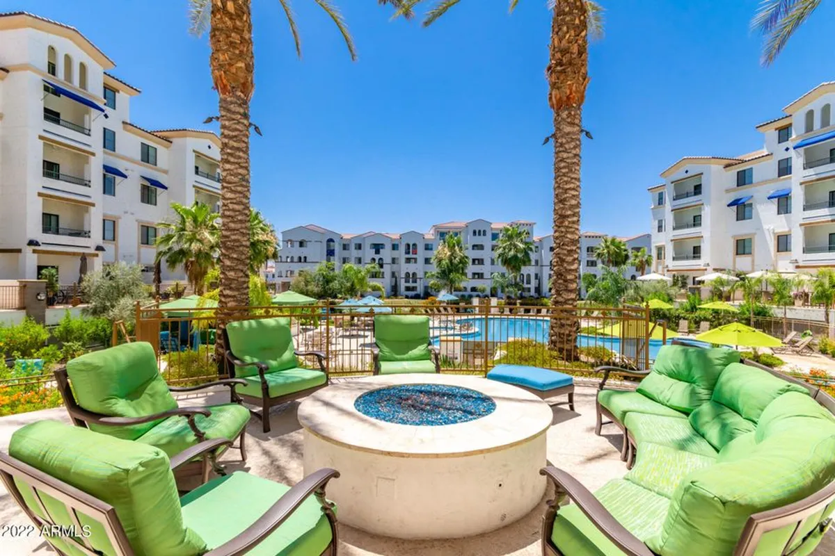A stylish outdoor fire pit surrounded by green lounge chairs and a swimming pool, set against the backdrop of palm trees. The scene is both inviting and social, suggesting evening gatherings and cozy moments outdoors.