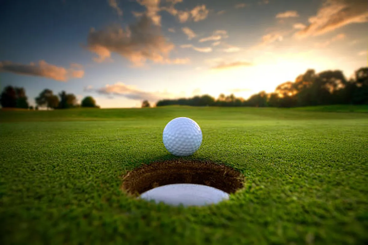 A close-up of a golf ball poised at the edge of a perfectly manicured hole, surrounded by lush green grass. The shot is tranquil and inviting, encapsulating the serenity and appeal of a high-quality golf experience.
