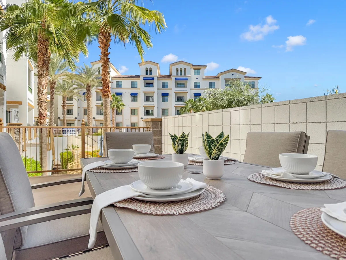 An inviting outdoor dining area with a table set for meals, surrounded by palm trees and with the building in the background. The relaxed setting suggests an ideal space for hosting sunset cocktails or brunches with friends, echoing the owner's mention of an expansive patio.