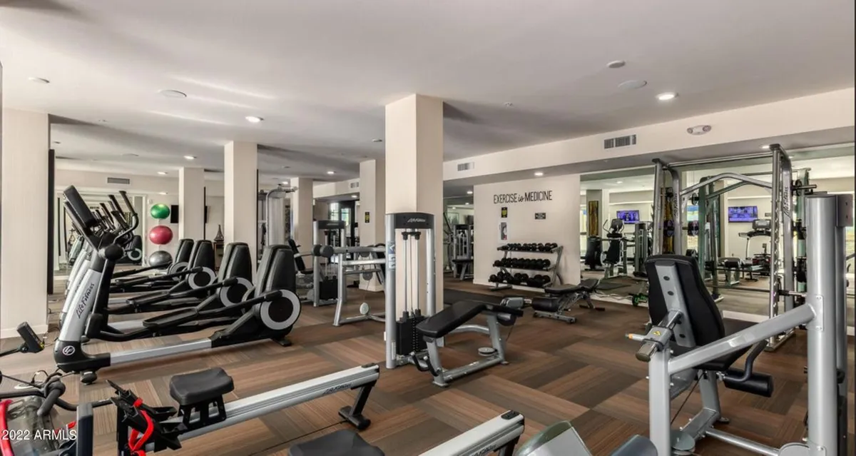 A bright, modern gym featuring a variety of exercise machines, free weights, mirrored walls, and open space for workouts or group fitness classes. The design is contemporary and motivating.
