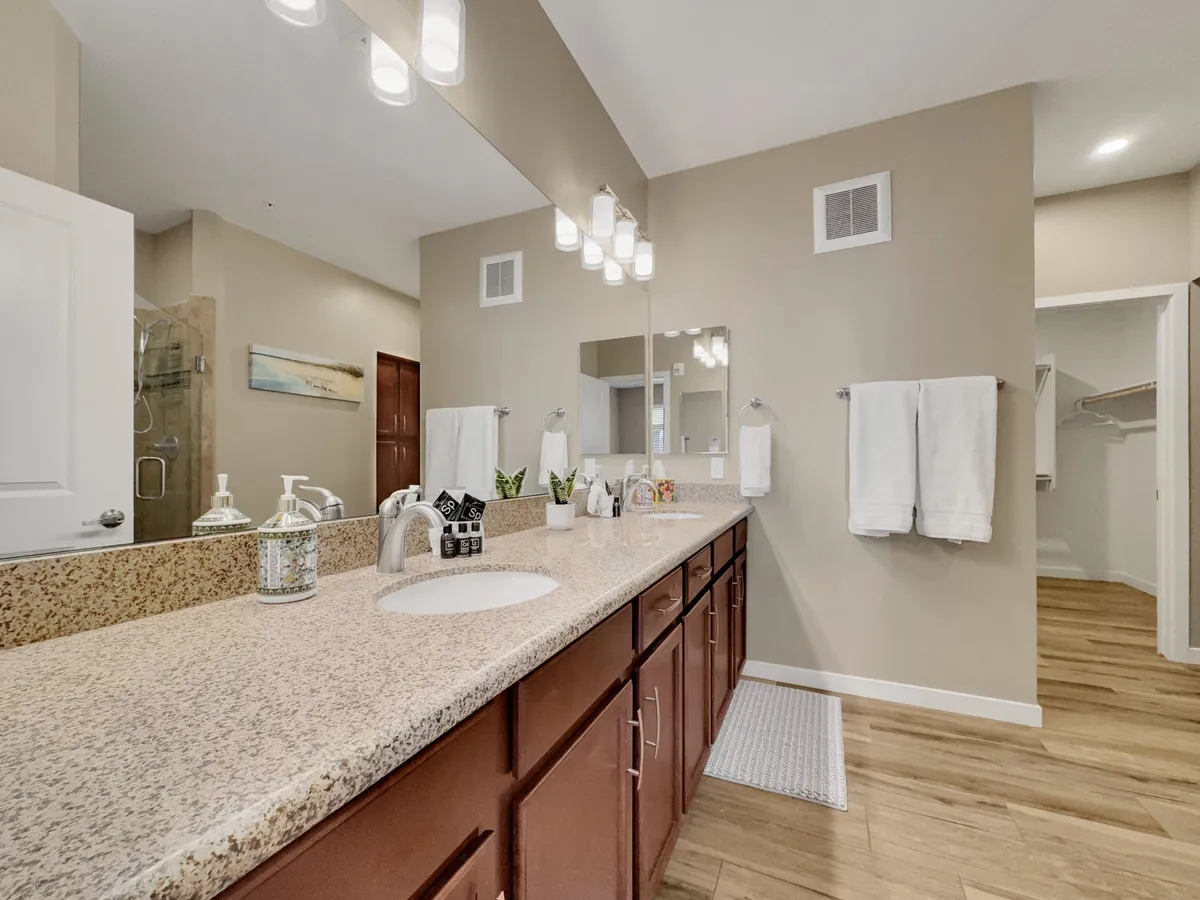 A modern bathroom with a granite countertop, dual sinks, large mirror, stylish lighting fixtures, and decorative touches. The space is bright, spotless, and spa-like, inviting relaxation and self-care.