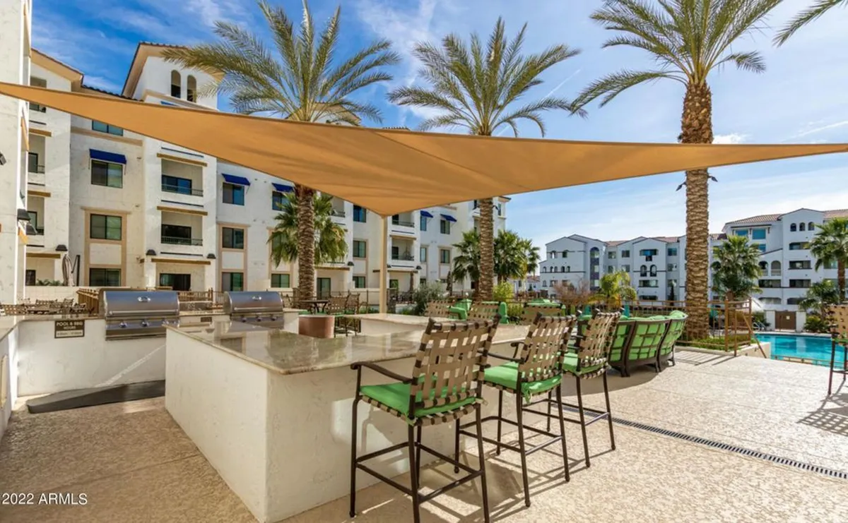 An inviting outdoor grill area with bar seating, tropical landscaping, and a sparkling swimming pool in the background. The scene captures a sociable, resort-style atmosphere for barbecues and gatherings.