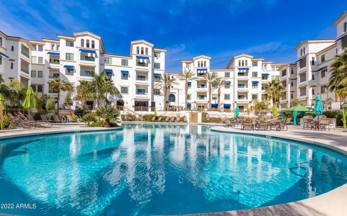 A resort-style swimming pool area framed by palm trees and flanked by lounge chairs and balconies. The scene exudes relaxation, leisure, and the vibrant, social atmosphere typical of upscale condo amenities.