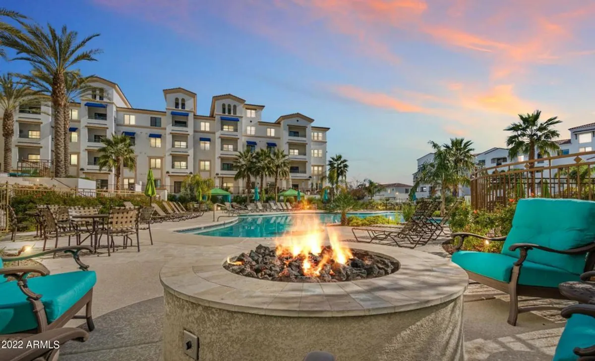 This image captures an expansive outdoor area featuring a modern fire pit surrounded by plush lounge chairs, all set beside a sparkling swimming pool framed with palm trees and the building’s facade. The scene is illuminated by the warm glow of sunset, inviting both social and tranquil moments.