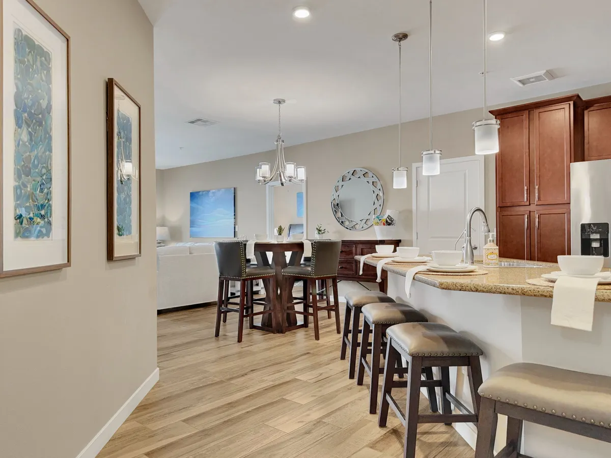 A warm, welcoming space with a kitchen island, dining table, stylish artwork, and modern lighting fixtures. The scene suggests both functionality for cooking and an inviting area for entertaining or enjoying a meal.
