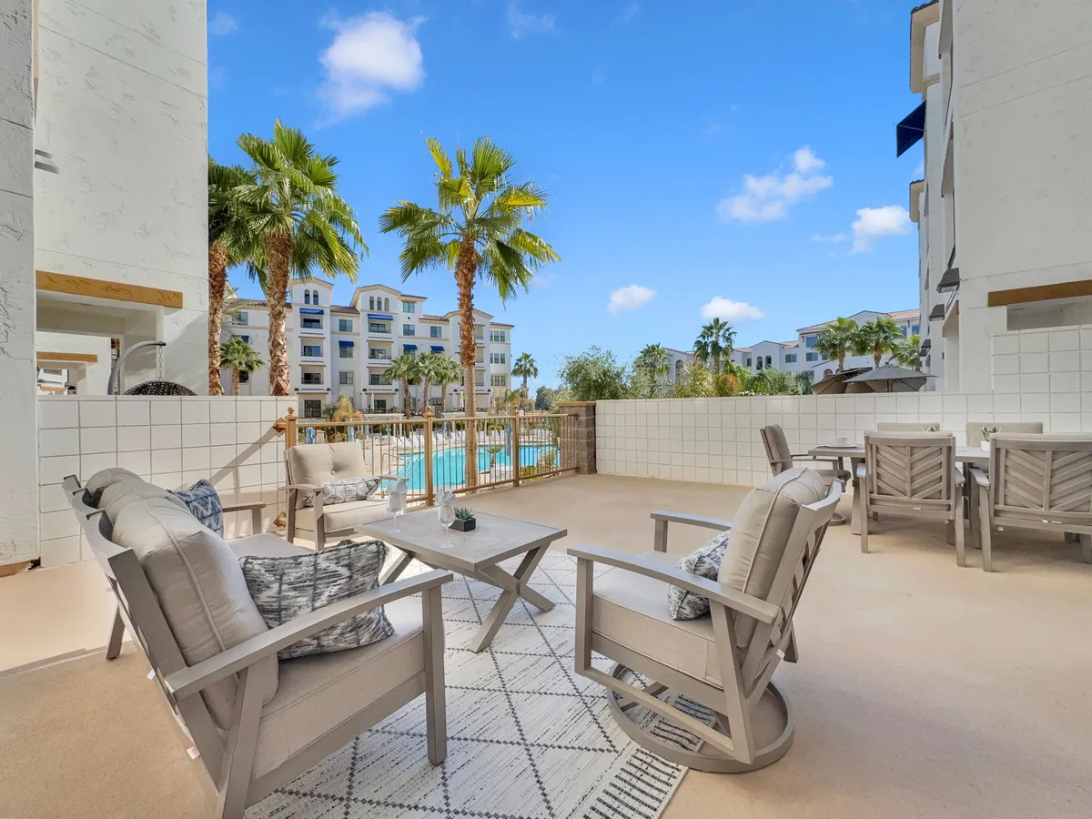 An inviting outdoor lounge area with modern seating and a nearby dining table, all set beside a glistening swimming pool framed by tropical palm trees. The setup encourages both casual relaxation and lively gatherings, in view of the water.