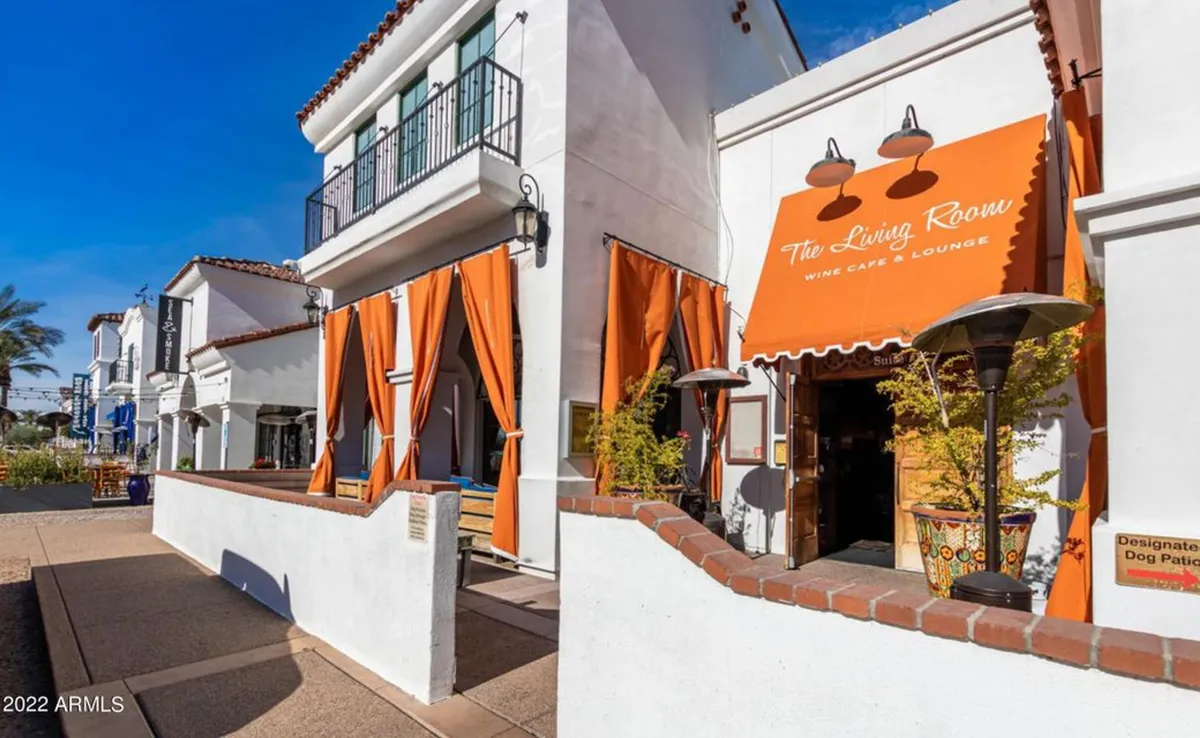 The welcoming entrance to 'The Living Room' café is adorned with orange curtains, signage, and an inviting outdoor dining area. The space radiates a sense of community and is clearly designed for casual meet-ups, dining, and relaxed social gatherings.